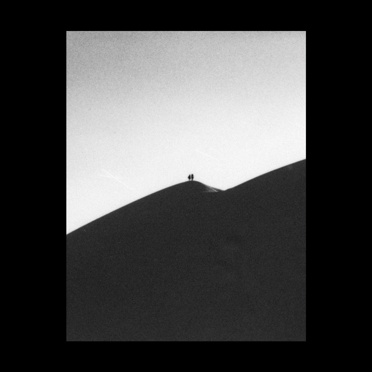 A black and white photographic print of two silhouettes on a sand dune.