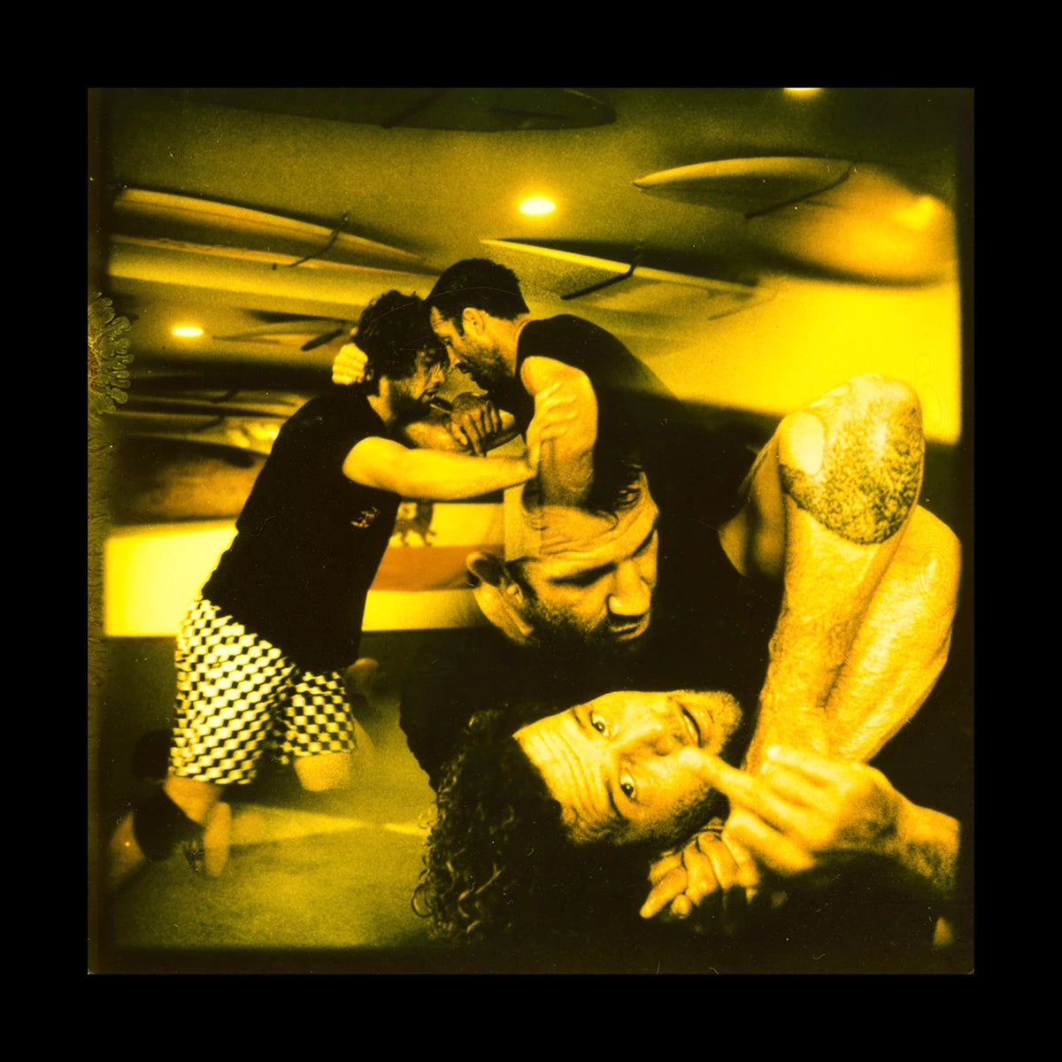 Photographic print of grappling training, collaged with an image of a grappler giving the middle finger. Yellow tinted photo.